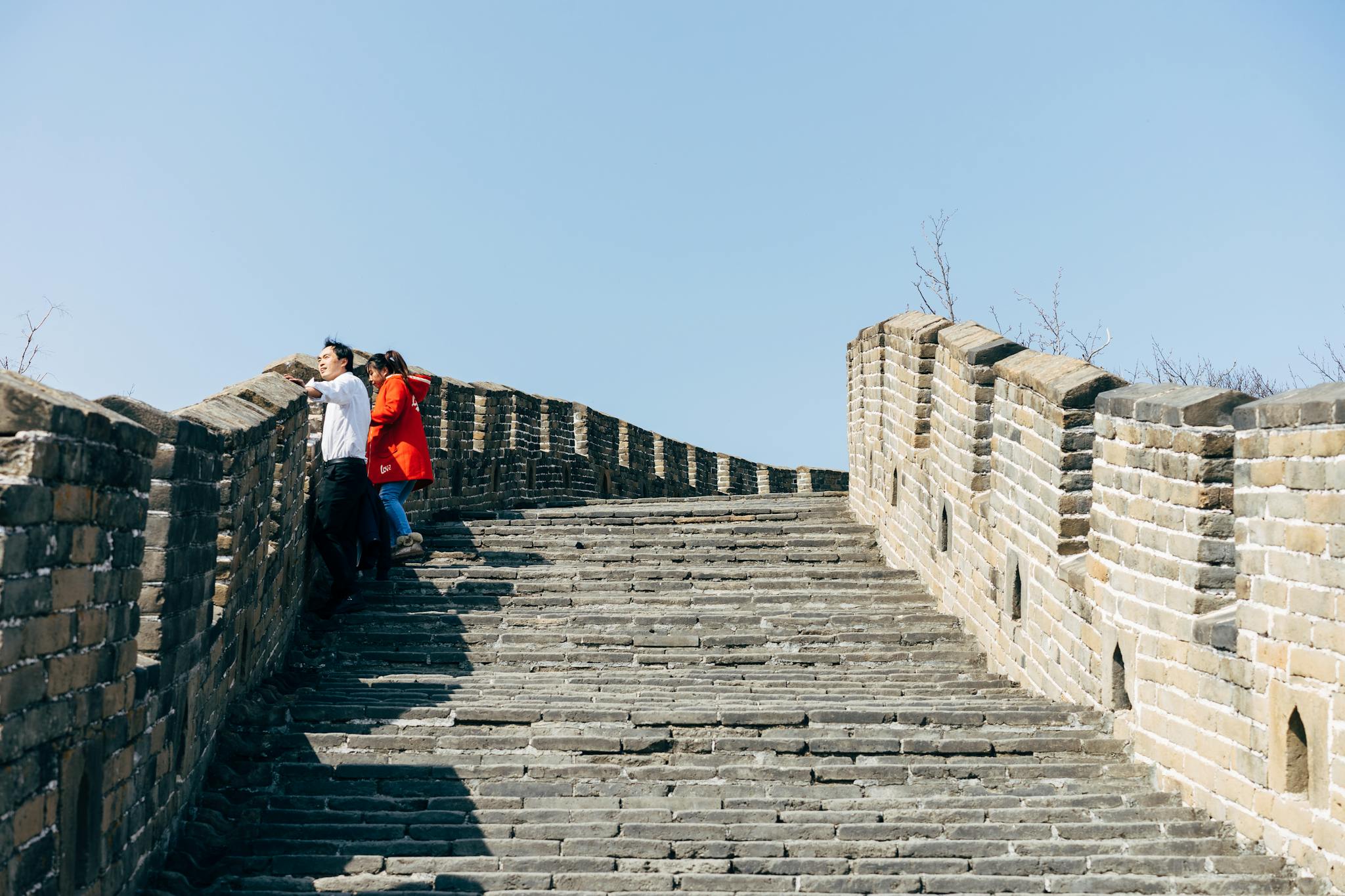 Tourists explore the historic Great Wall of China under clear blue skies, capturing its architectural beauty.